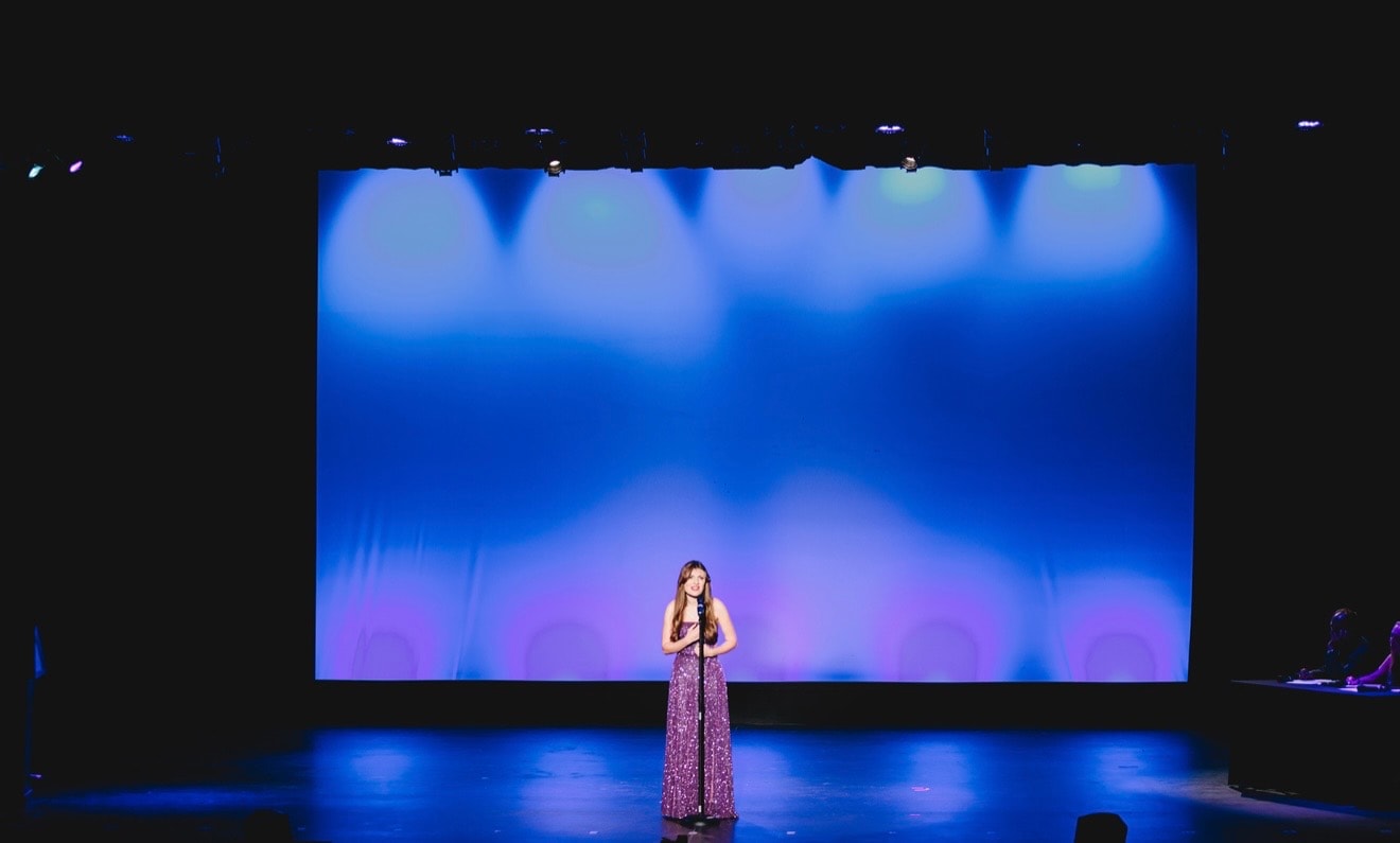 Savannah Lynn performing on stage in a purple gown with blue LED backdrop